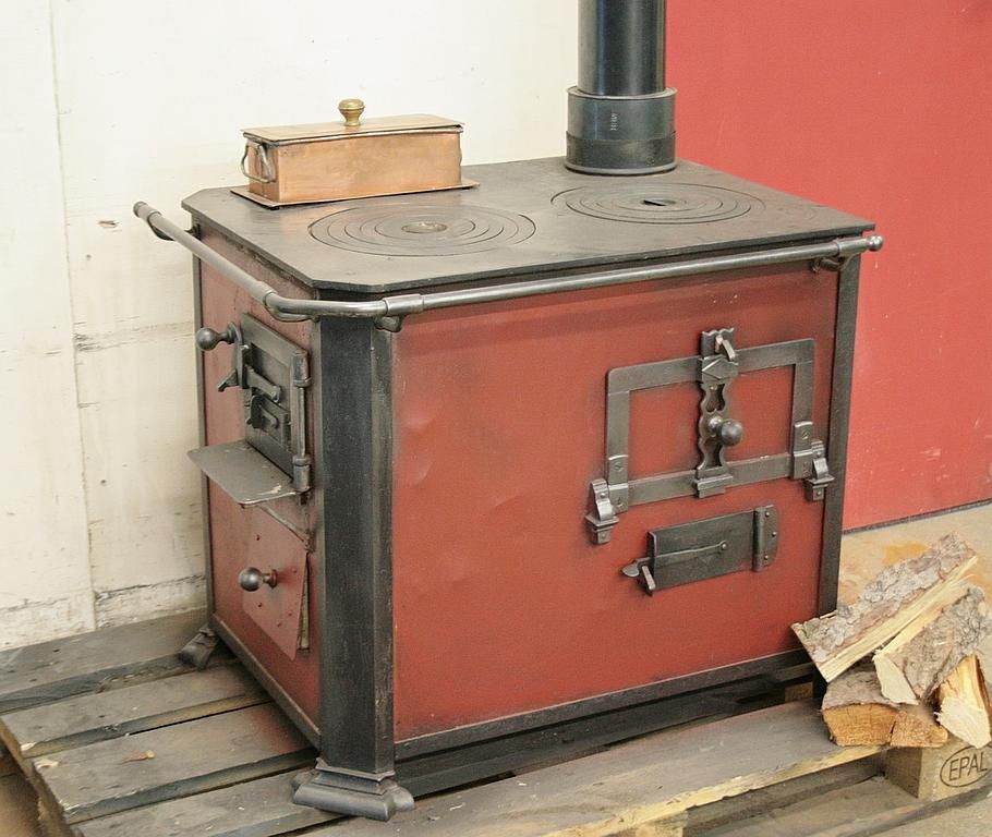 Fourneau rustique n° 1351 – Perler Ofen / Fourneau d’angle avec foyer sur le côté gauche, avec deux plaques de cuisson, panache en cuivre et four. Les boutons, les supports de barres et la barre porte-torchon peuvent être neufs en laiton ou nickelés.