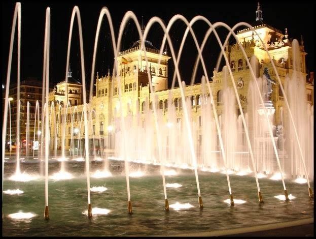 Una fuente se ilumina por la noche frente a un edificio.