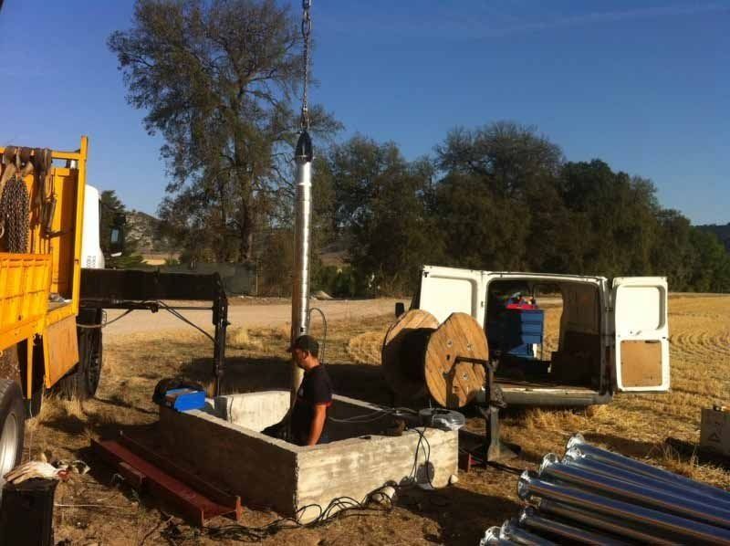 Un hombre se sienta en un agujero junto a un camión amarillo y una camioneta blanca.