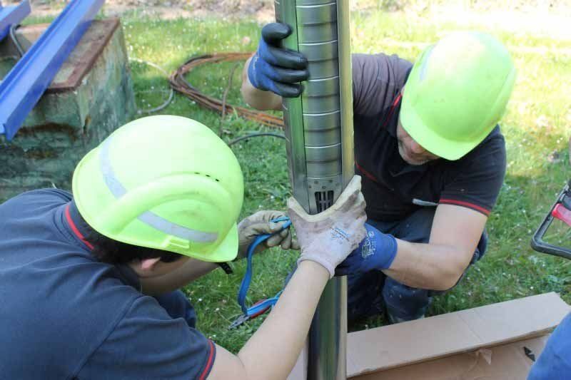 Dos hombres que llevan cascos de seguridad están trabajando en una tubería.