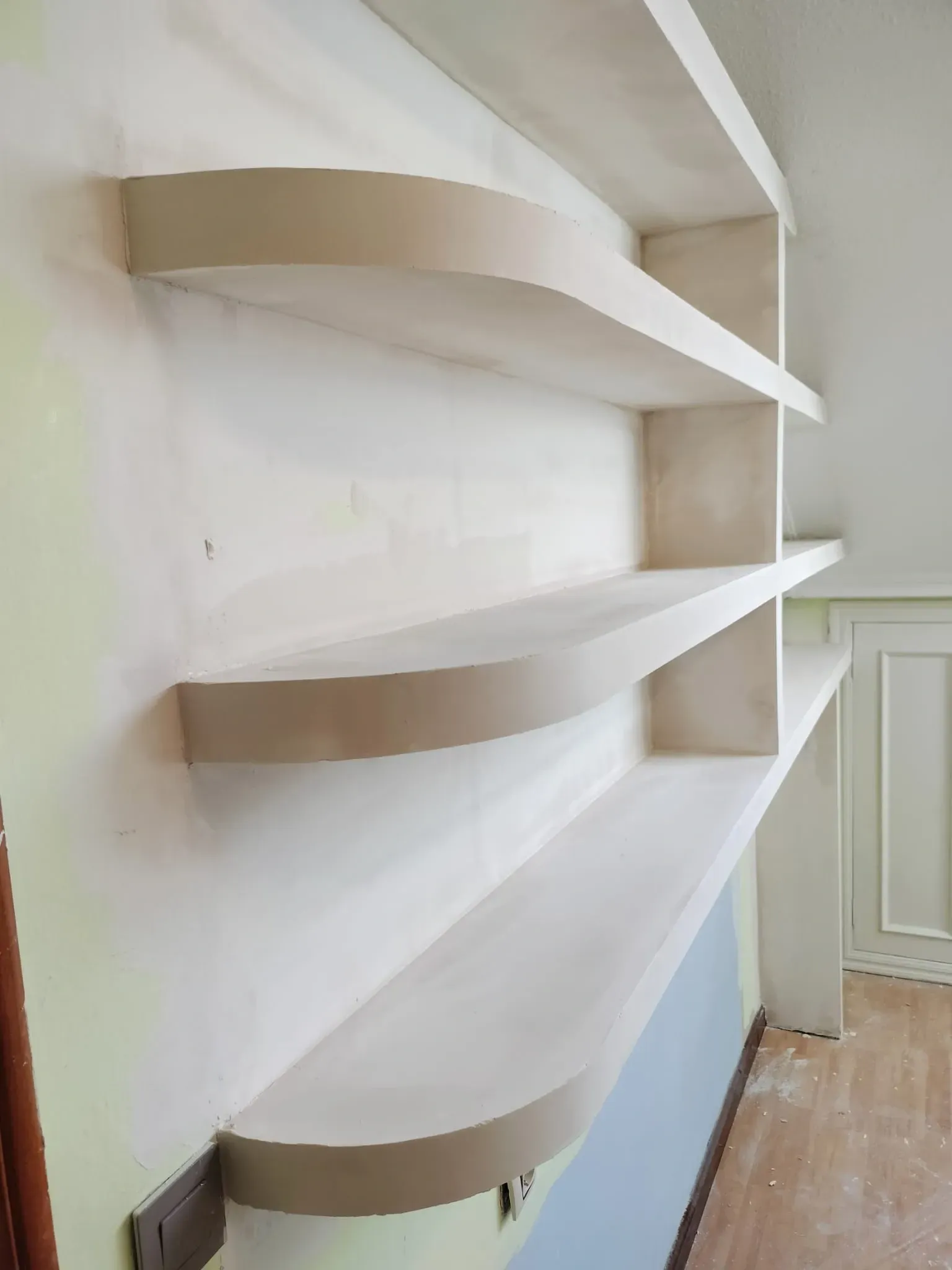 Tres estantes curvos de madera de color claro, sin acabado