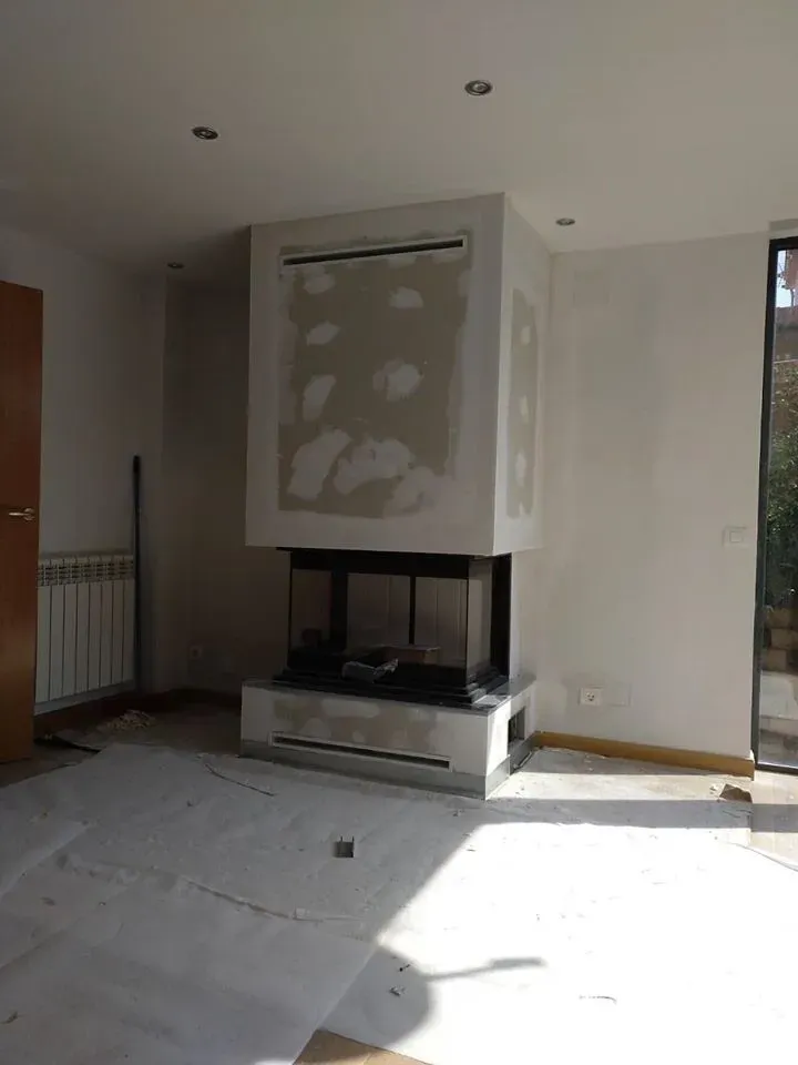 Una chimenea central en construcción en una habitación con paredes blancas y un revestimiento protector en el suelo.