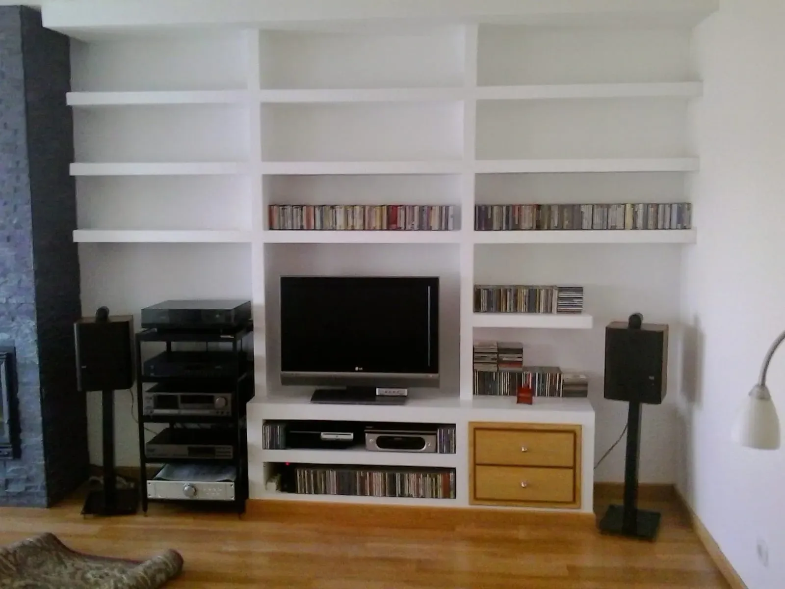 Un mueble blanco empotrado con una estantería, un equipo de música, dos cajones y estantes llenos de CD en una sala de estar.