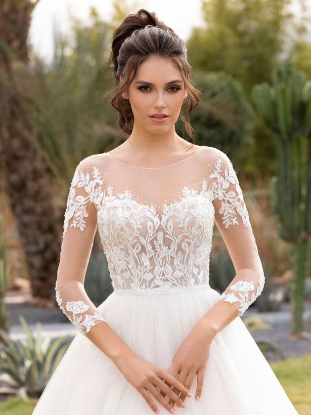 Eine Frau trägt ein weißes Hochzeitskleid mit langen Ärmeln.