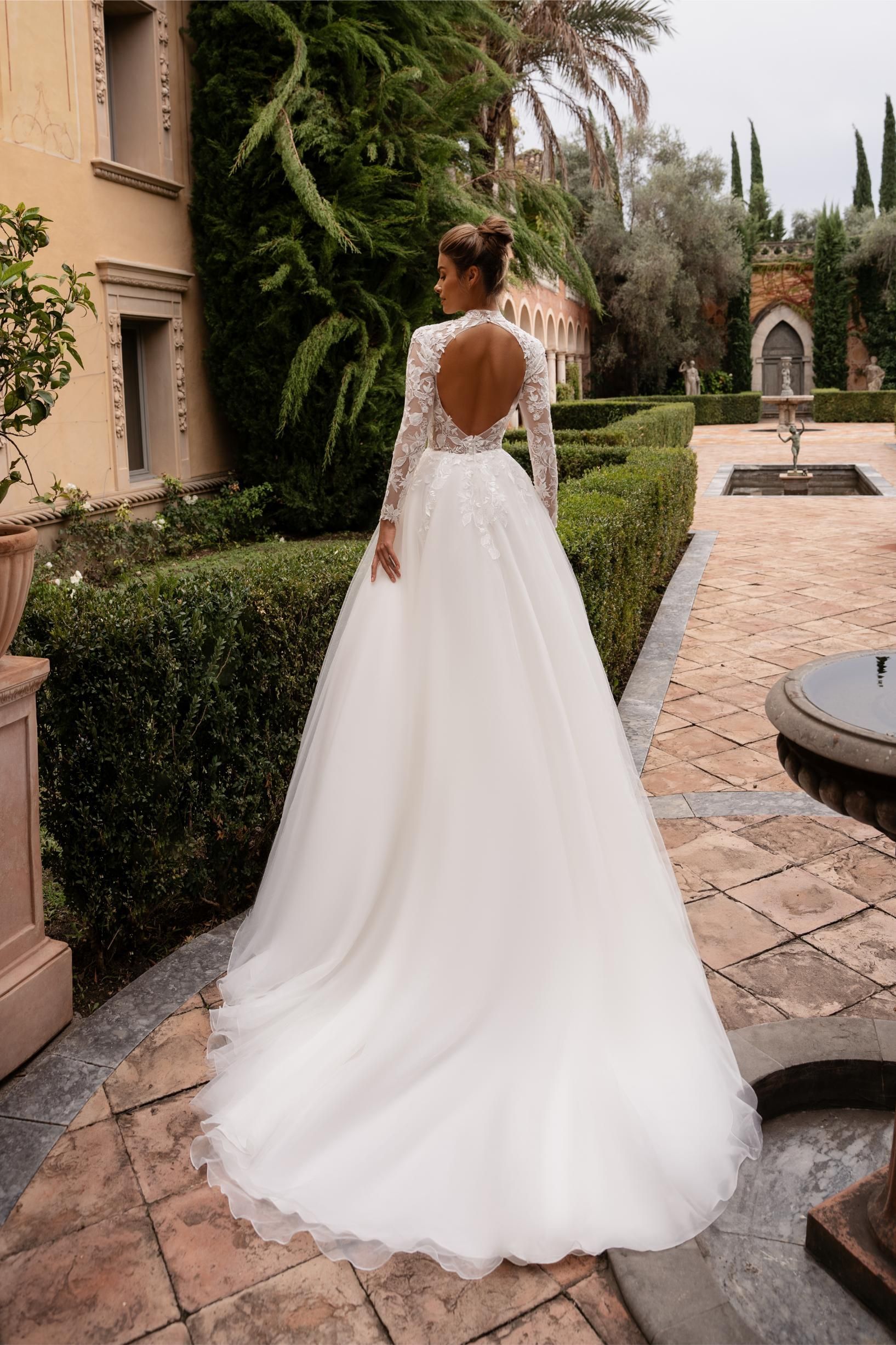 Eine Frau in einem weißen Hochzeitskleid steht vor einem grauen Hintergrund.