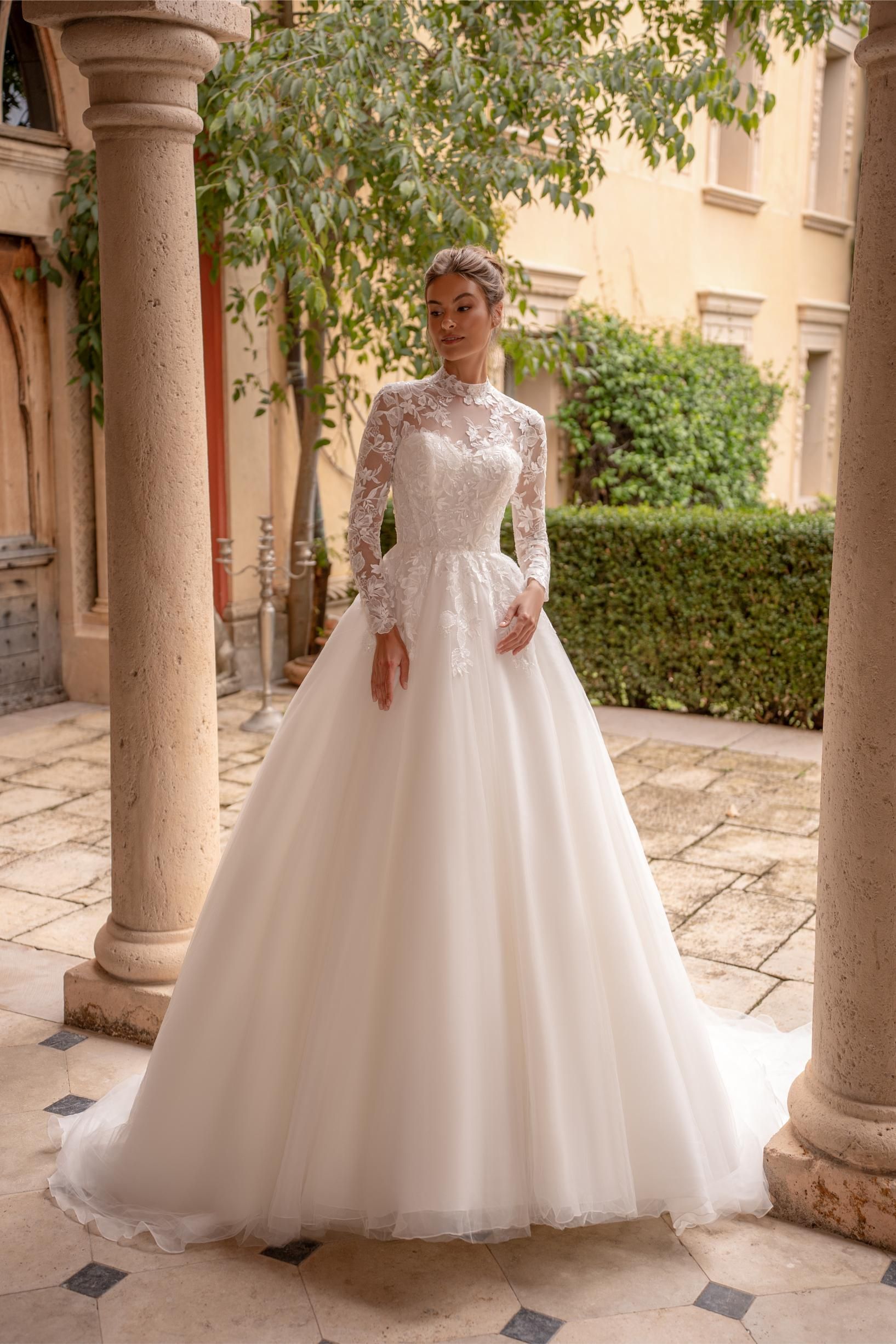 Eine Frau in einem weißen Hochzeitskleid steht vor einem grauen Hintergrund.