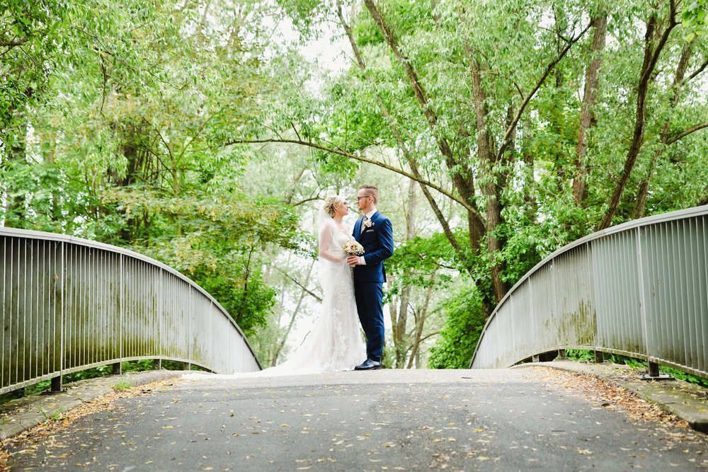 Eine Braut und ein Bräutigam stehen auf einer Brücke im Wald.