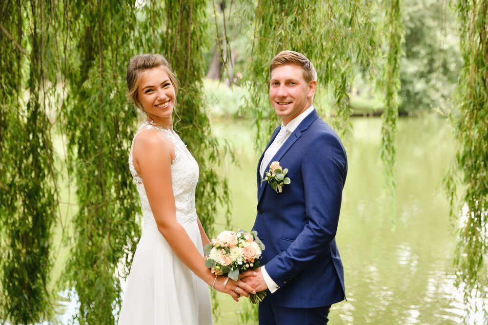 Eine Braut und ein Bräutigam posieren für ein Foto unter einer Weide.