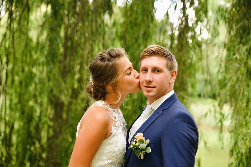 Eine Braut und ein Bräutigam küssen sich unter einer Weide.