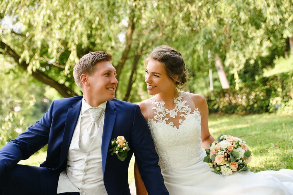 Eine Braut und ein Bräutigam sitzen unter einem Baum in einem Park.