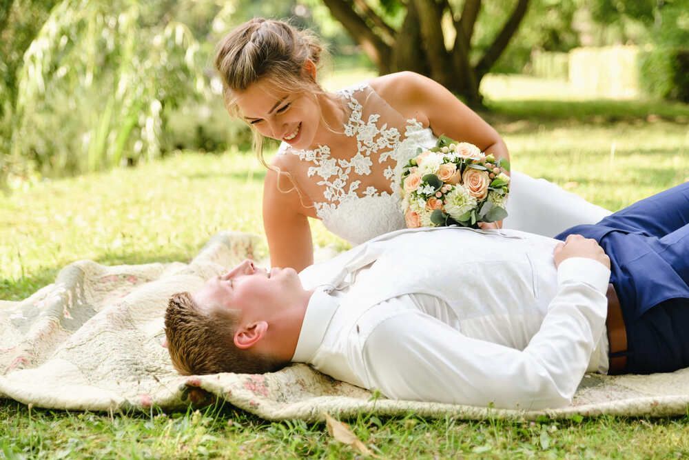 Braut und Bräutigam liegen auf einer Decke im Gras.