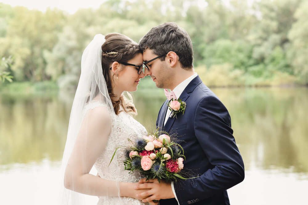 Eine Braut und ein Bräutigam schauen sich vor einem See an.