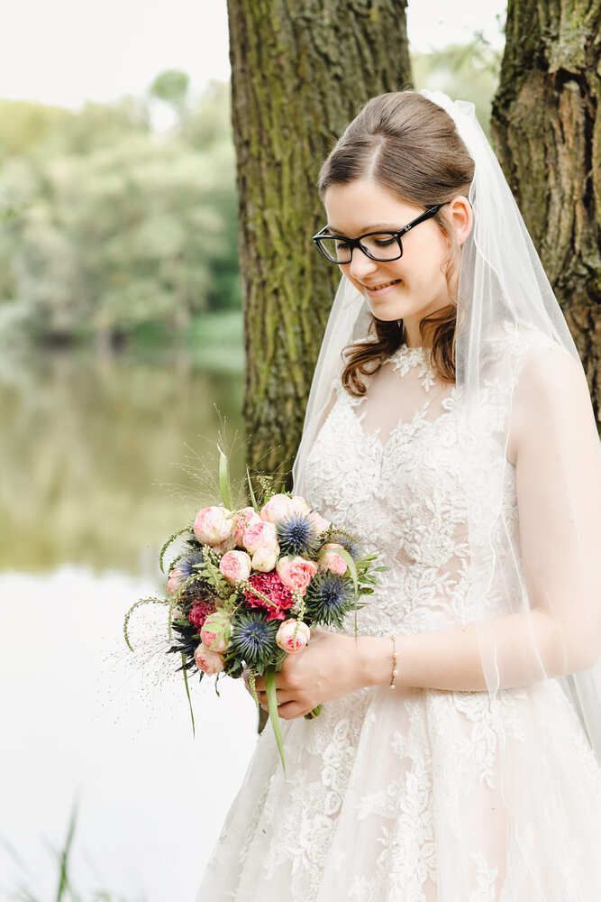 Die Braut trägt eine Brille und hält einen Blumenstrauß.
