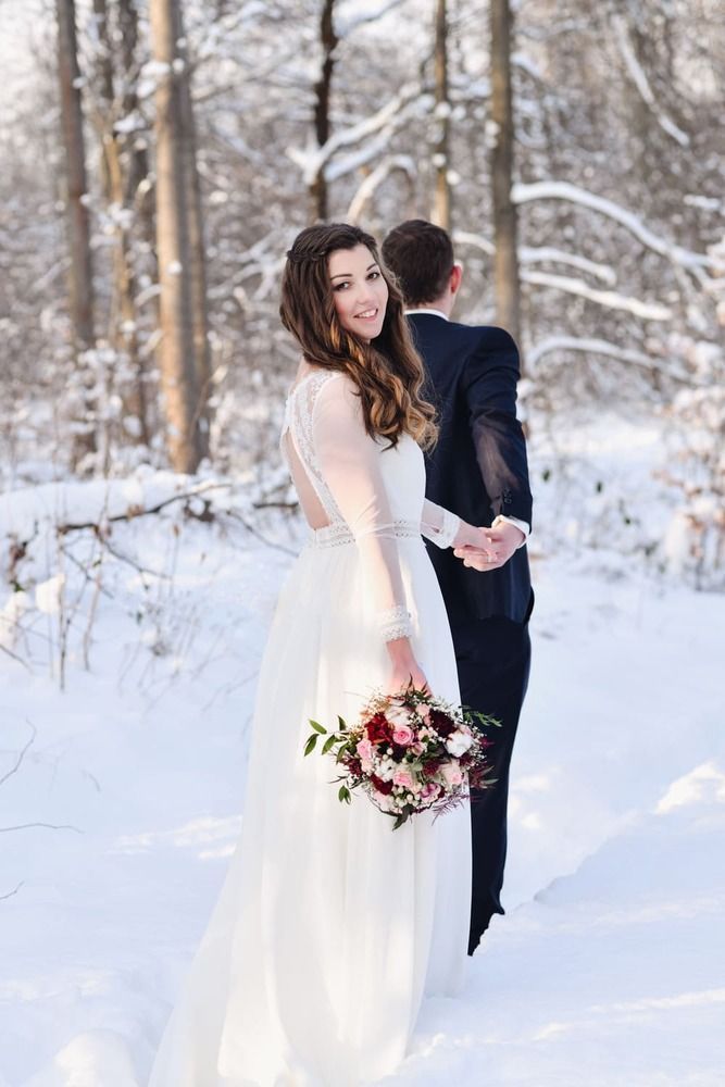 Eine Braut und ein Bräutigam stehen Händchen haltend im Schnee.