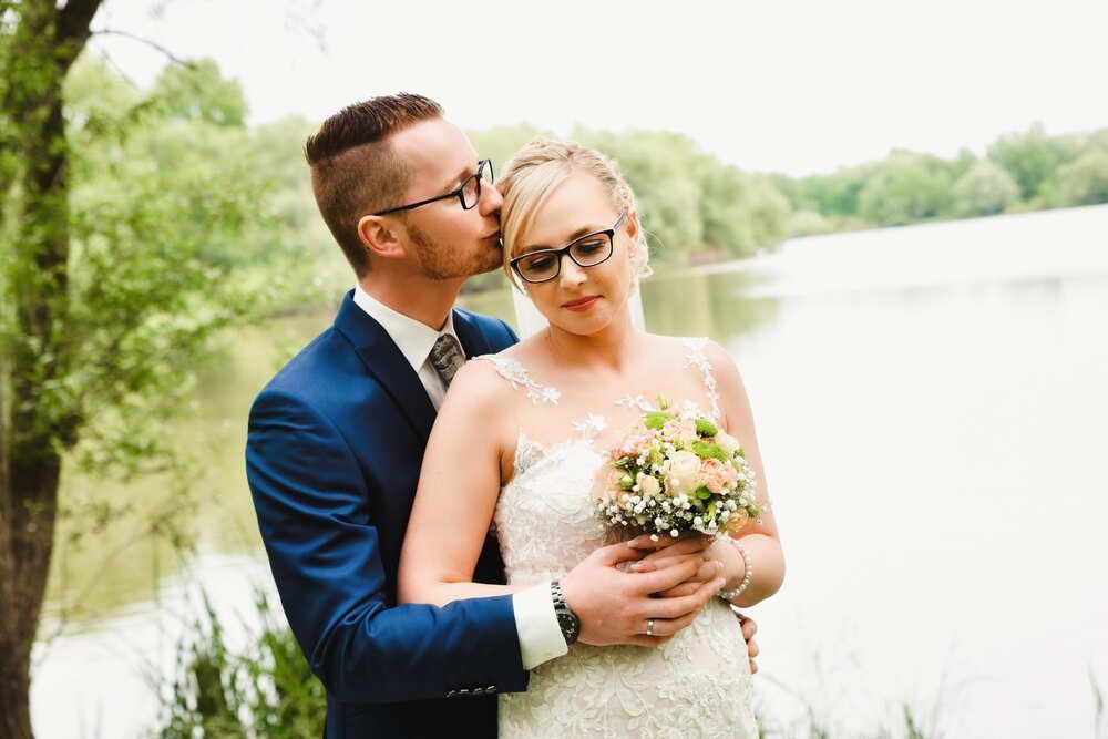 Eine Braut und ein Bräutigam posieren für ein Foto vor einem See.