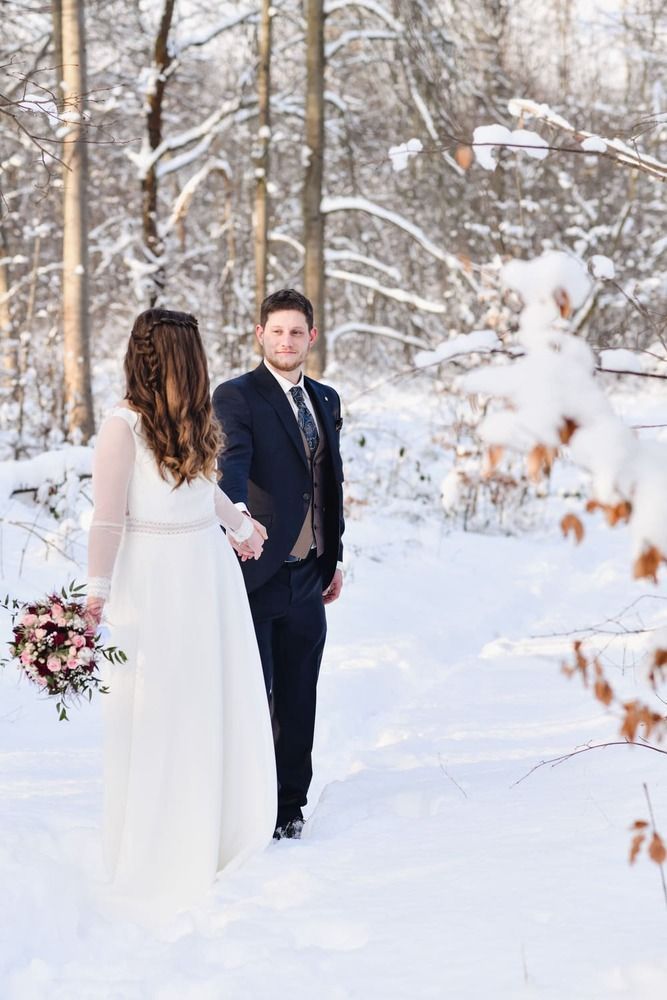 Eine Braut und ein Bräutigam stehen Händchen haltend im Schnee.