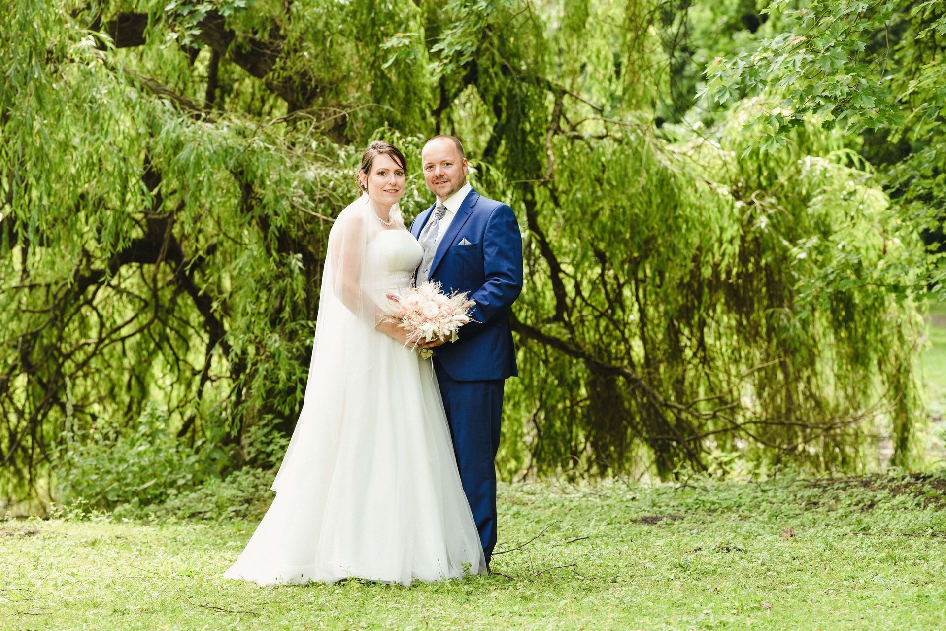 Eine Braut und ein Bräutigam posieren für ein Foto vor einer Weide.