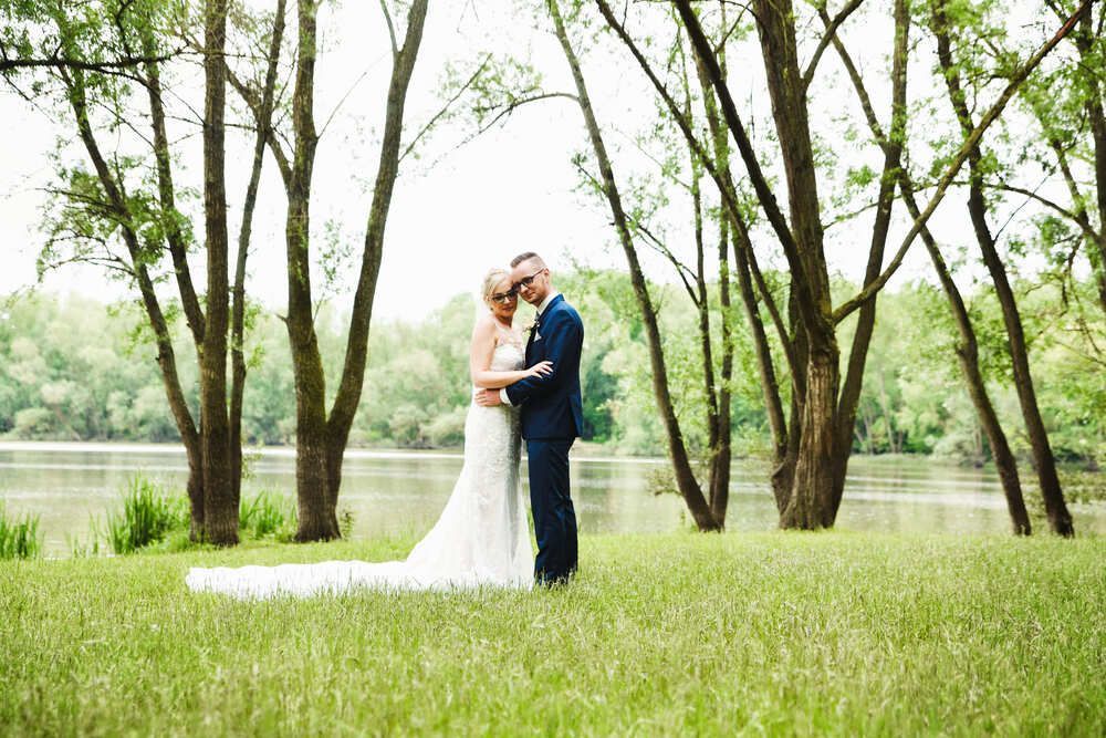 Eine Braut und ein Bräutigam stehen auf einem Feld neben einem See.