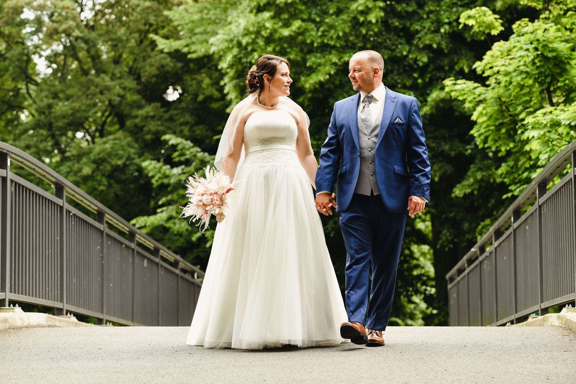 Eine Braut und ein Bräutigam gehen Hand in Hand über eine Brücke.