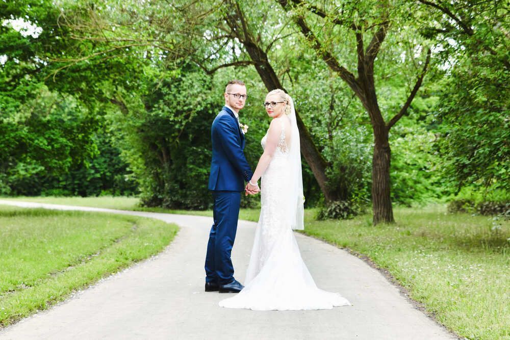 Eine Braut und ein Bräutigam stehen Händchen haltend auf einem Weg.