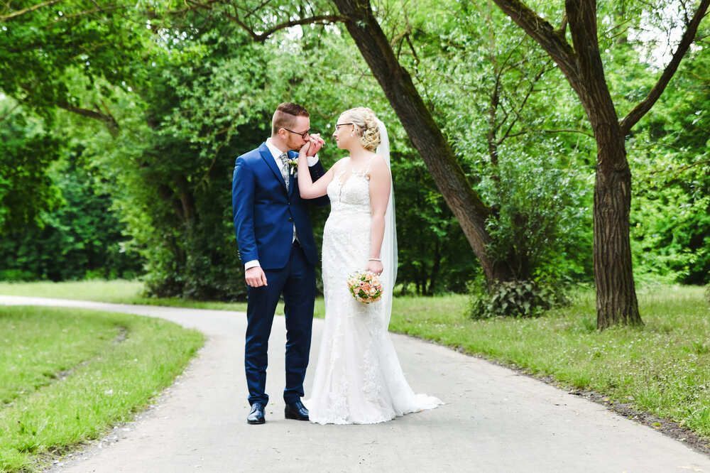 Eine Braut und ein Bräutigam küssen sich auf einem Weg in einem Park.