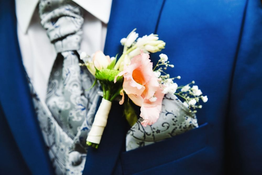 Ein Mann in einem blauen Anzug und einer Krawatte hält einen Blumenstrauß in seiner Tasche.