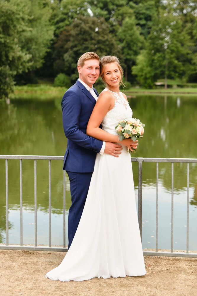 Eine Braut und ein Bräutigam posieren für ein Foto vor einem See.