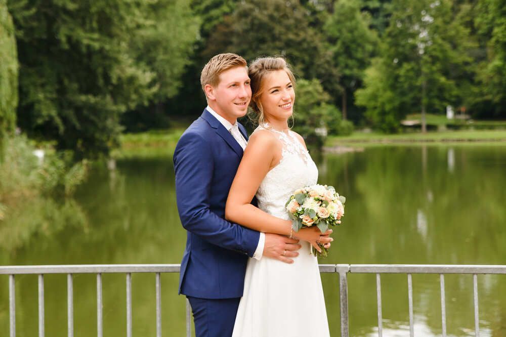 Eine Braut und ein Bräutigam posieren für ein Foto vor einem See.