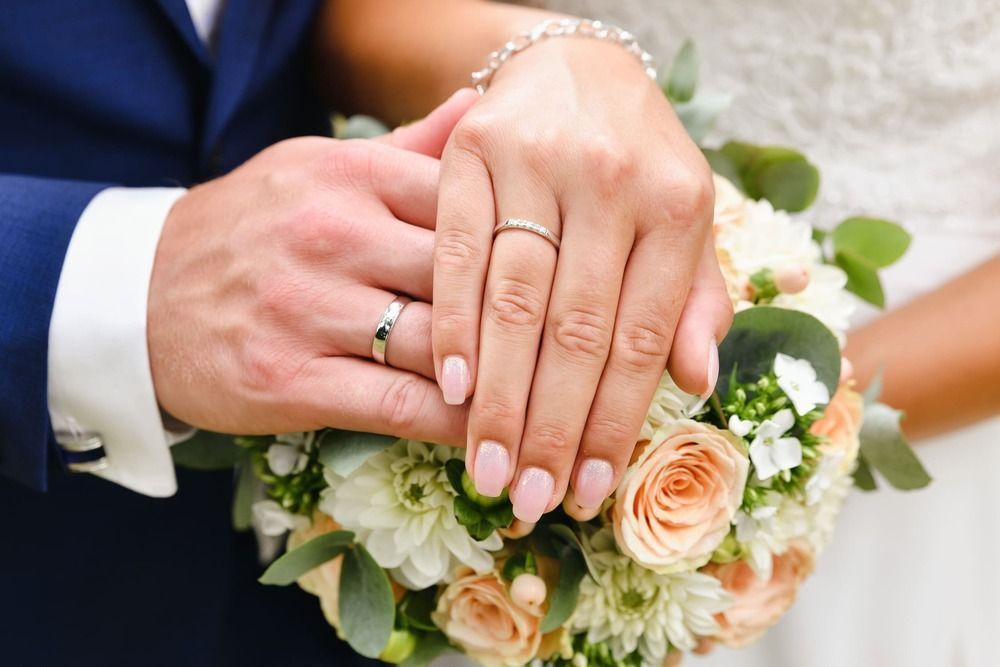 Eine Braut und ein Bräutigam halten Händchen und tragen ihre Eheringe an den Fingern.