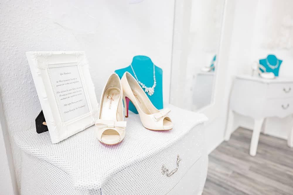 Ein Paar weiße High Heels steht auf einer weißen Kommode neben einem Bilderrahmen.