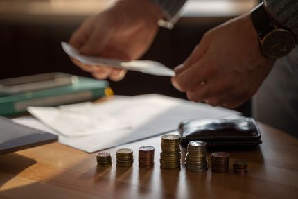 Unas manos contando monedas sobre un escritorio junto a papeles, una cartera y un reloj, bajo una luz cálida.