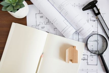 Escritorio con cuaderno abierto, lápiz, planta y planos arquitectónicos enrollados con herramientas de dibujo.