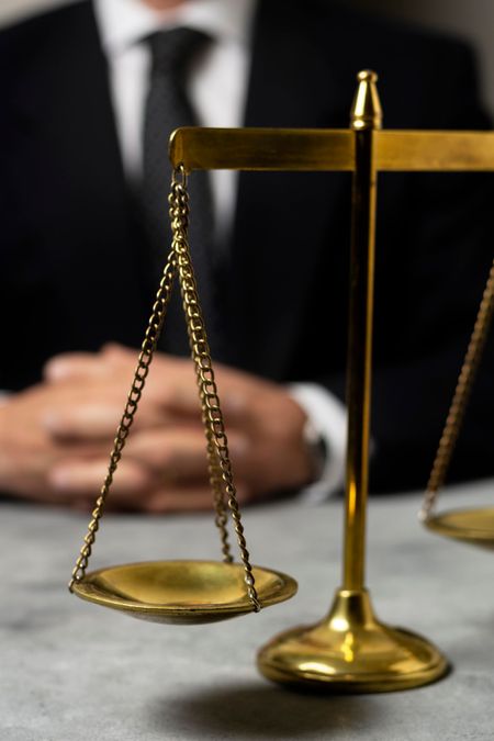 Balanza de latón sobre un escritorio con una persona desenfocada vestida con traje detrás.