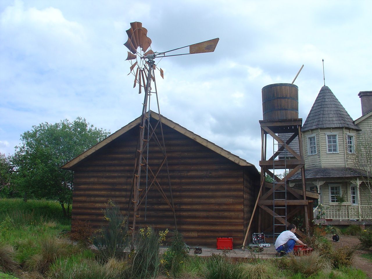 Éolienne posée devant d'une maison en bois et son château d'eau