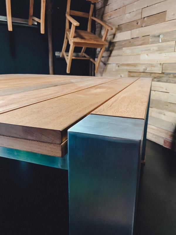 Ein Holztisch mit Metallbeinen und ein Stuhl im Hintergrund