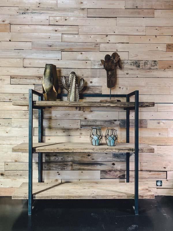 Vor einer Holzwand steht ein Holzregal mit Metallrahmen.