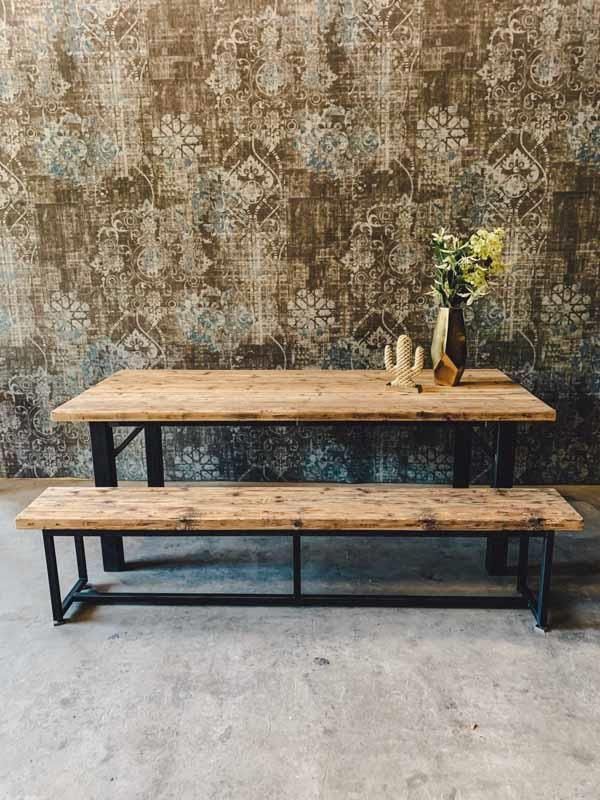 Ein Holztisch mit einer Bank und einer Vase mit Blumen darauf.