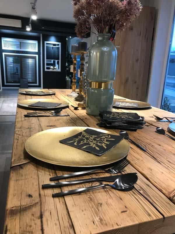 Ein Holztisch mit Tellern, Besteck und einer Vase mit Blumen darauf.