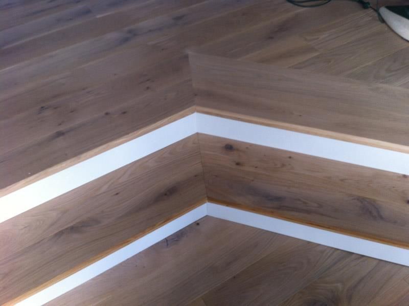Eine Ecke eines Holzbodens mit weißen Zierleisten