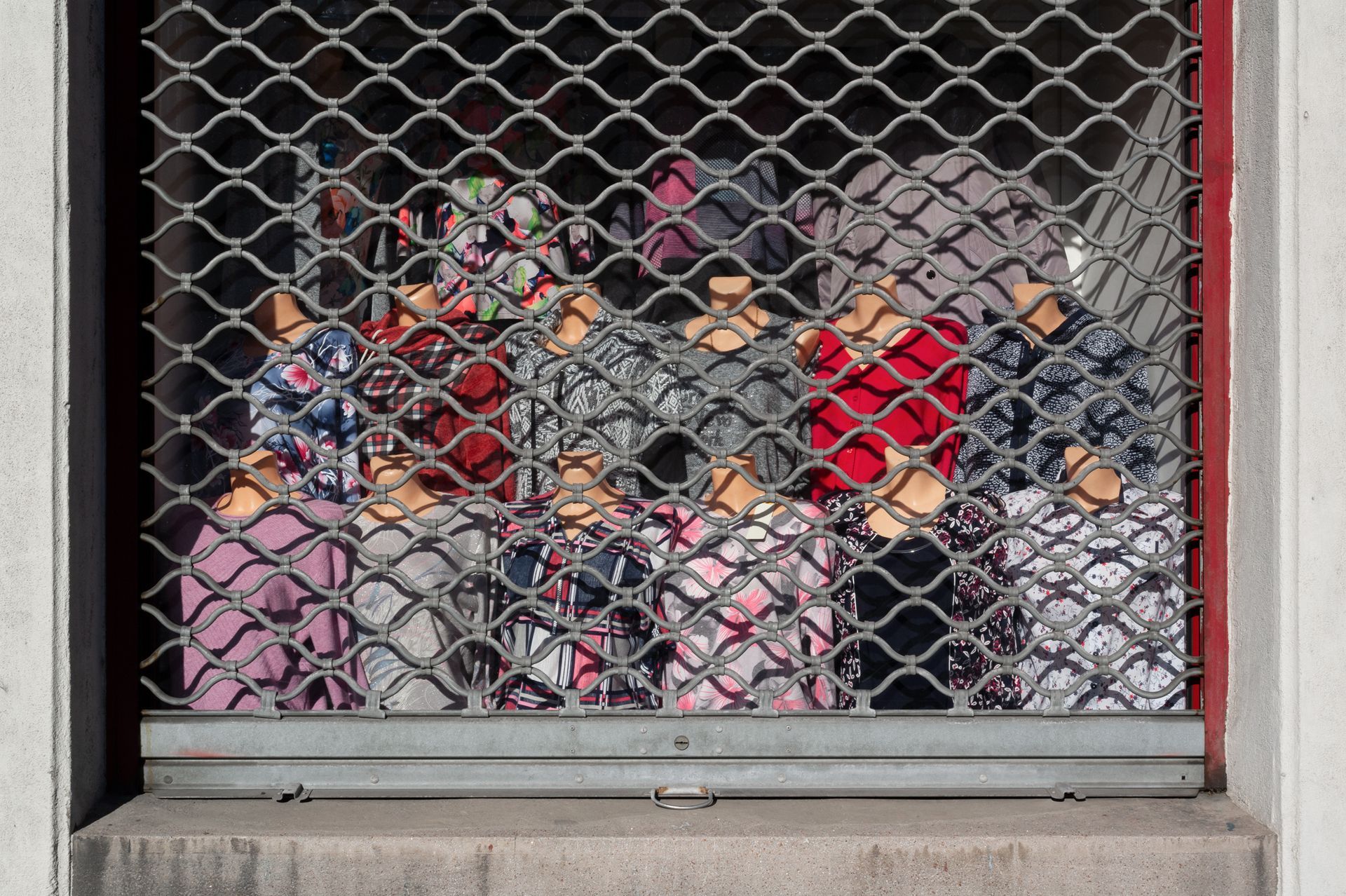 Des personnes derrière une grille de sécurité métallique, entassées dans une vitrine ou devant une fenêtre.