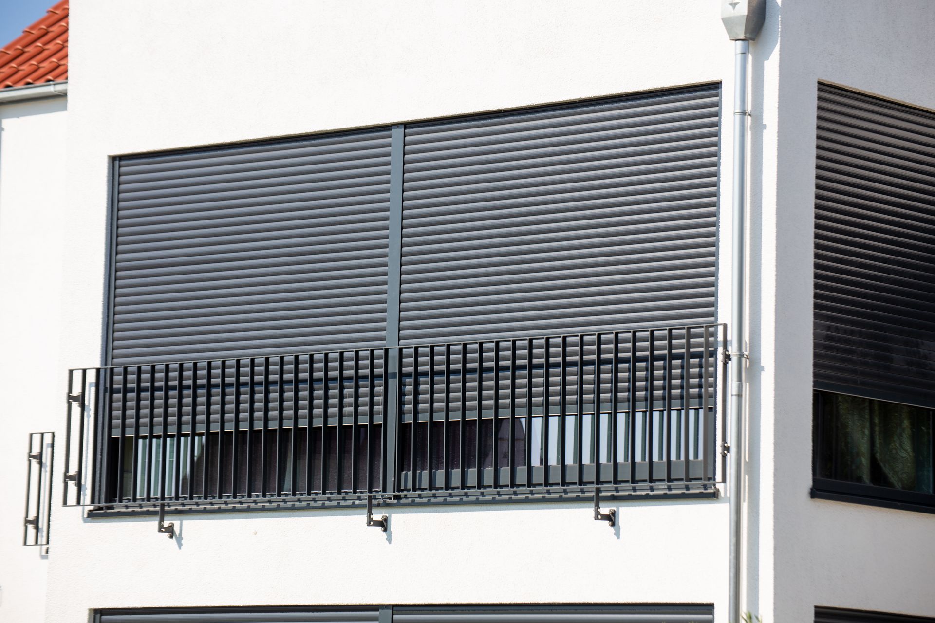 Façade d’un bâtiment avec des volets gris fermés et un garde-corps de balcon noir