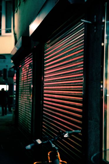 Vitrine sombre avec un rideau métallique fermé, éclairée par des néons rouges et verts dans la nuit