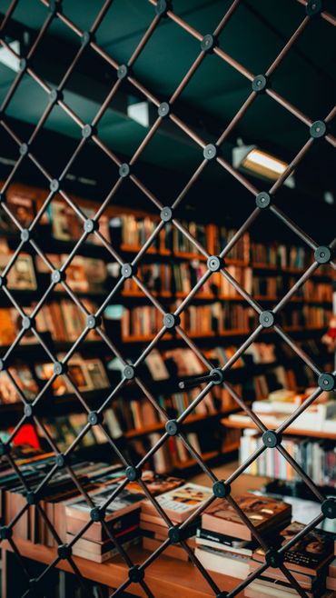 Des étagères et des tables aperçues à travers un grillage, dans un espace de bibliothèque ou de café chaleureux à l’éclairage tamisé