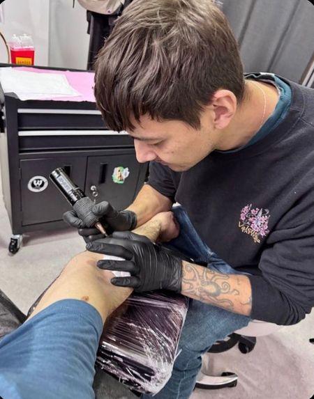 Un hombre se está haciendo un tatuaje en la pierna de una persona.