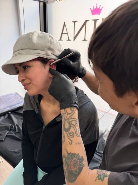 Una mujer se está perforando la oreja mediante un tatuador.