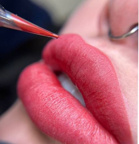 Una mujer se aplica lápiz labial rojo en los labios con un pincel.