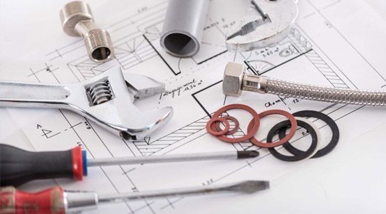 Herramientas y accesorios de fontanería en los planos, incluyendo llave inglesa, cinta métrica, piezas de tubería y anillos roscados.