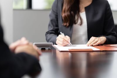 Eine Frau sitzt an einem Tisch und schreibt auf einem Klemmbrett.