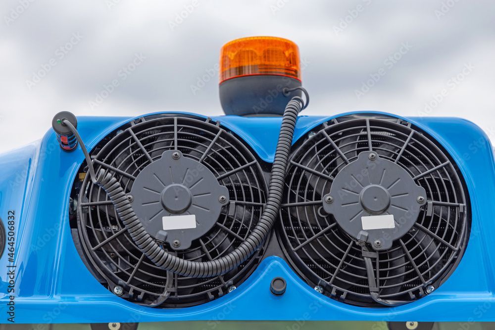 Machine bleue avec deux ventilateurs et un voyant d'avertissement orange sur fond de ciel nuageux.