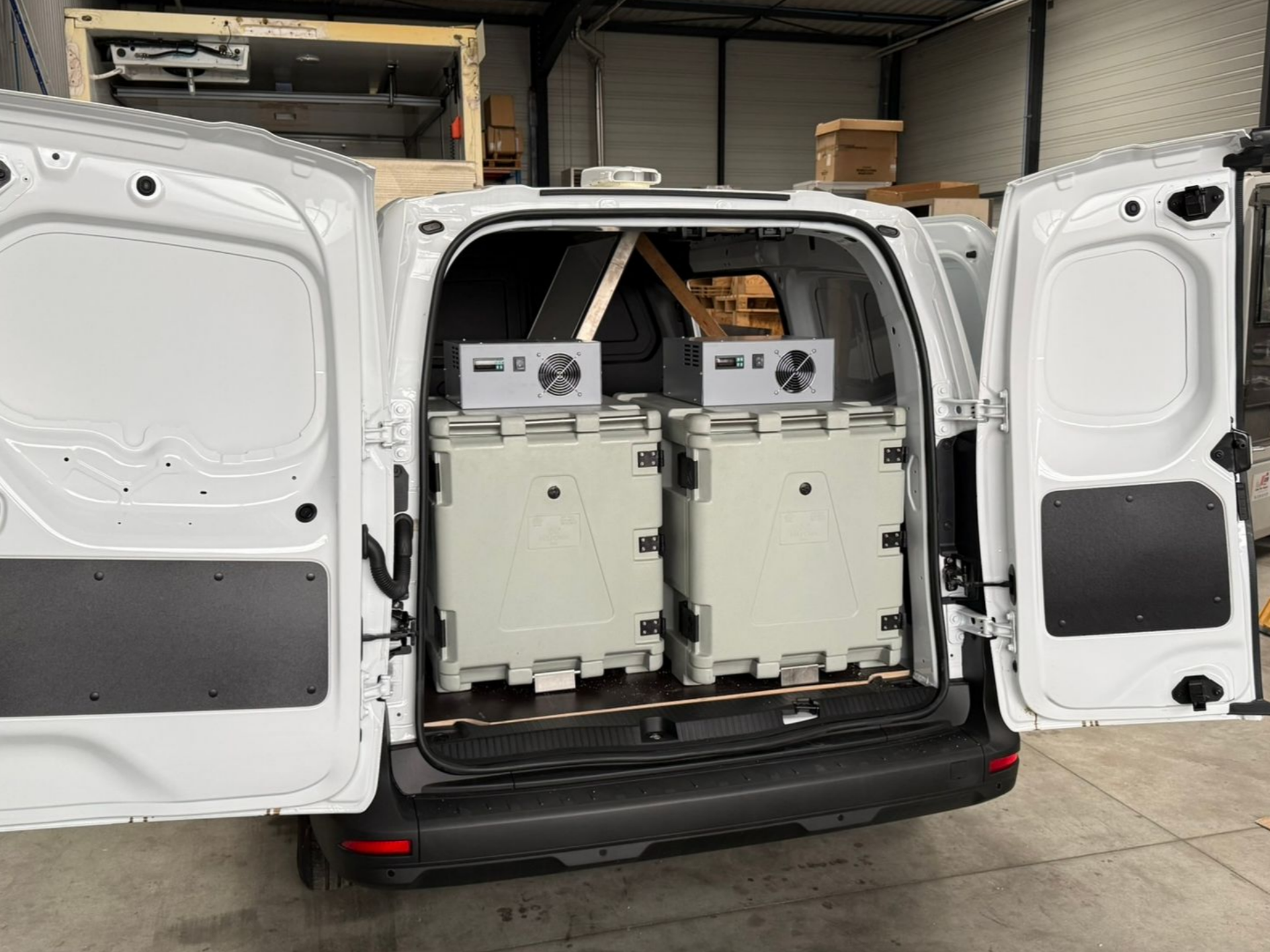L'arrière d'une camionnette blanche s'ouvre, révélant deux boîtes grises et deux machines à l'intérieur.